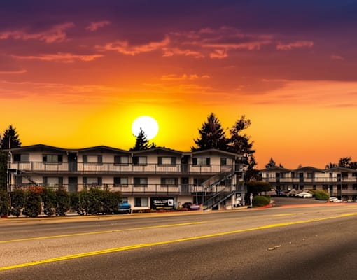 A sunset view of a street with apartment buildings and cars parked on the side.