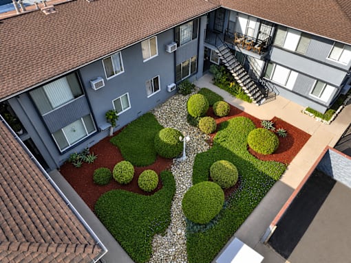 A building with a red roof and a courtyard with bushes and a staircase.