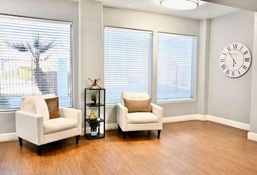 Two white chairs are placed in a room with a clock on the wall.