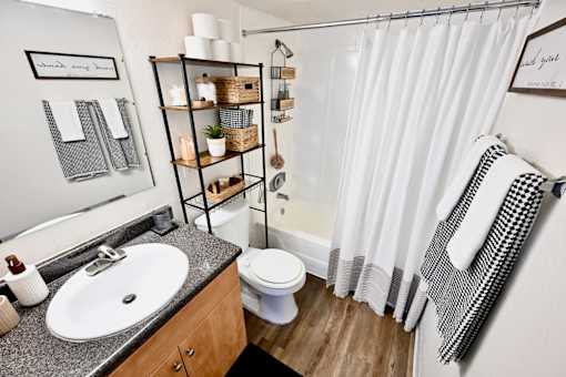 A bathroom with a white shower curtain, a white toilet, a sink, and a shelf with baskets and plants.