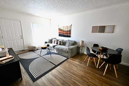 A living room with a black and white rug, a grey sofa, a black dining table and chairs, and a wooden floor.