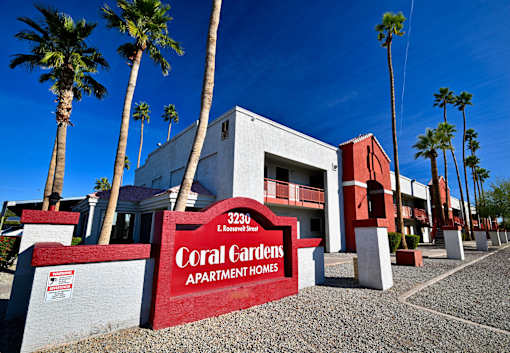 A sign for Coral Gardens Apartment Homes is in front of a building with palm trees.