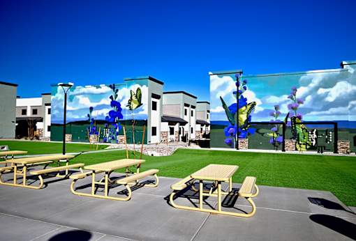 Picnic tables are set up on a concrete surface in front of a colorful mural.