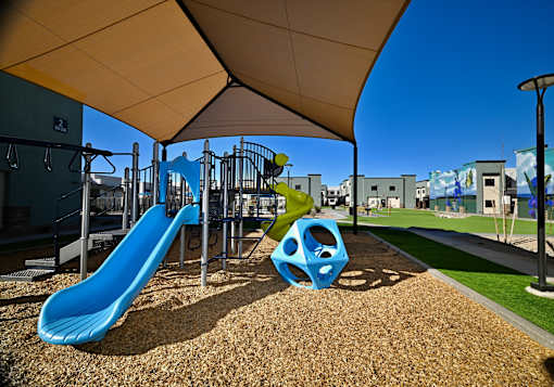 A playground with a blue slide and a brown sandbox under a canopy.