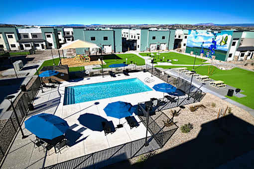 A pool with blue umbrellas and chairs is surrounded by a fence.