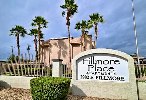 A sign for Fillmore Place Apartments stands in front of a building with palm trees.