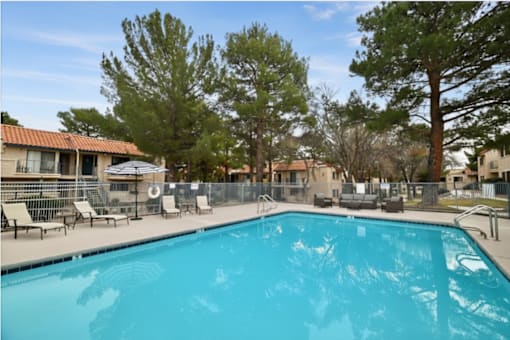 A swimming pool surrounded by trees and chairs.