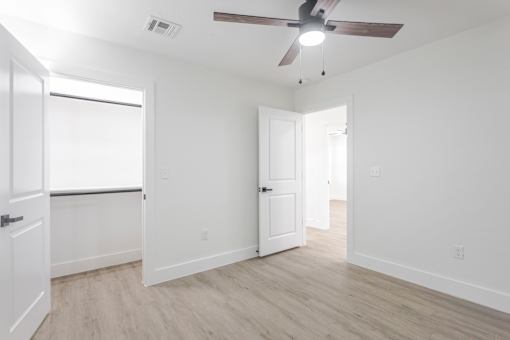A room with a ceiling fan and light, two doors, and a window.
