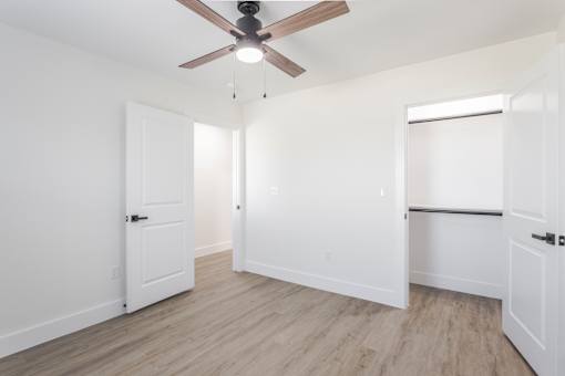 A room with a ceiling fan and light, white walls, and a wooden floor.