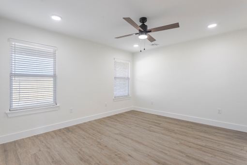 A room with a ceiling fan and two windows with blinds.
