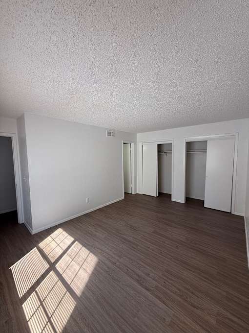 A room with wooden flooring and white walls with a window casting a shadow on the floor.