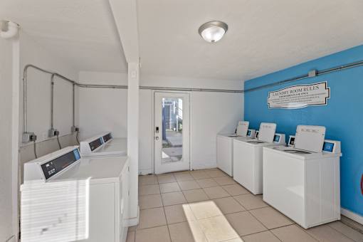 A laundromat with washers and dryers and a sign that says "Tailor Room Rules".