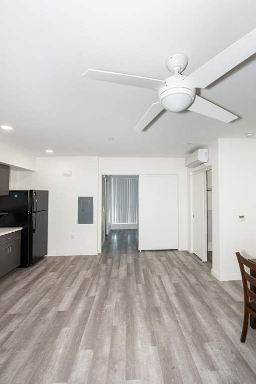 an empty living room with a ceiling fan and a kitchen