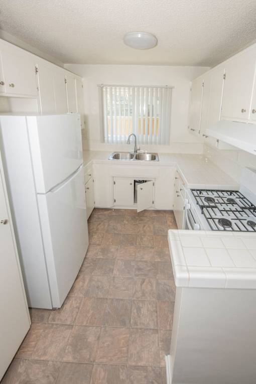 A kitchen with white appliances and brown tile flooring.