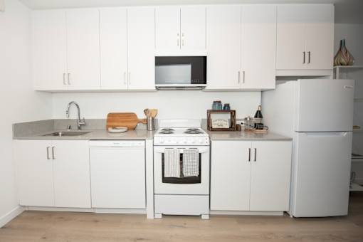 A white kitchen with a stove, sink, and cabinets.