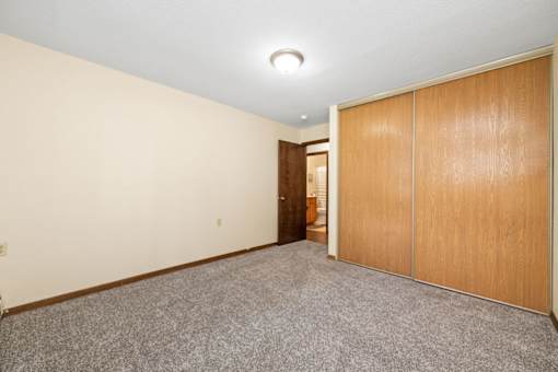 A room with a grey carpet and wooden wardrobes.