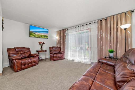 A living room with a brown leather couch and a flat screen TV mounted on the wall.