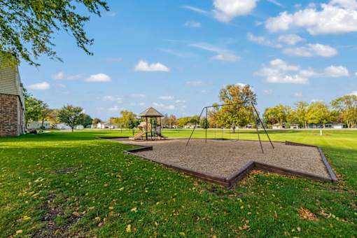 A playground with a swing set and a sandbox in the foreground.