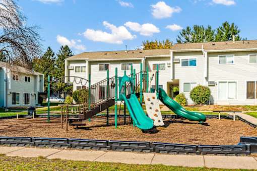 A playground with a green slide and a brown swing set.