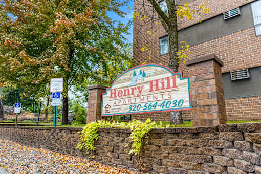 A sign for Henry Hill Apartments is displayed in front of a brick building.