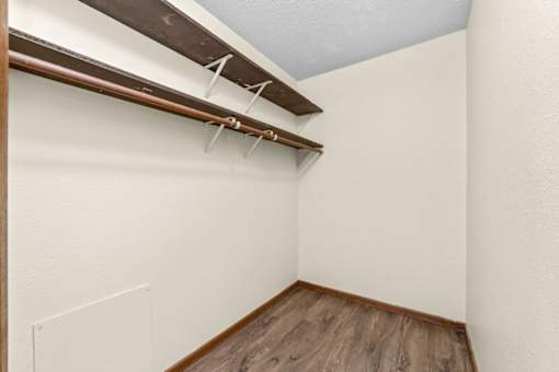 A small room with a wooden floor and a white wall with a shelf above it.
