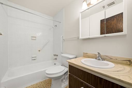 A white toilet sits under a white tiled shower in a small bathroom.
