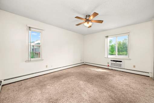 A room with a ceiling fan and two windows.