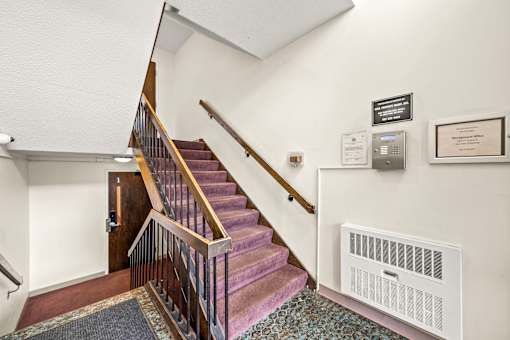 A staircase with a red carpet and a white wall with a framed certificate.