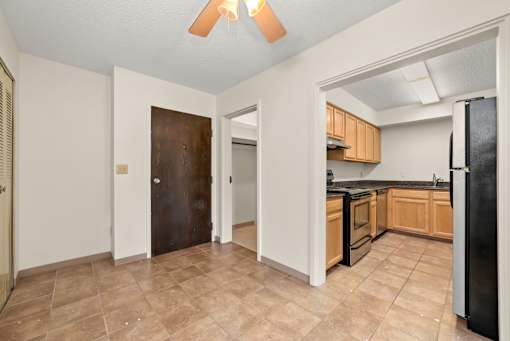 A kitchen with a black fridge and brown flooring.