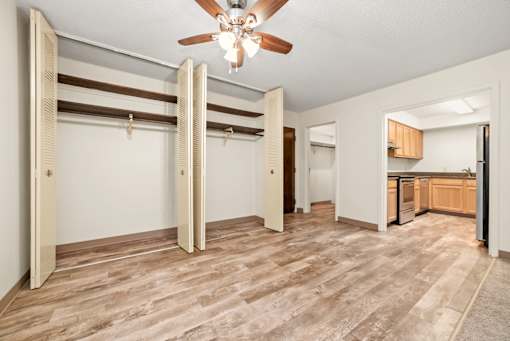 A room with a ceiling fan and a kitchen area in the background.