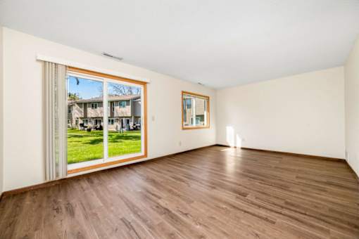 A room with wooden floors and a large window showing a view of a house.