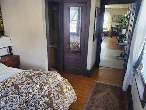 A bedroom with a bed, dresser, and a view of the living room through a door.