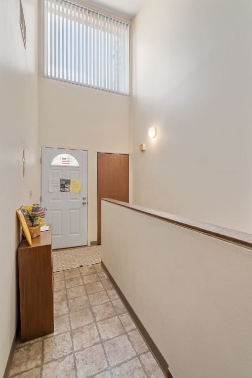 a hallway with white walls and a white door and a desk with a vase