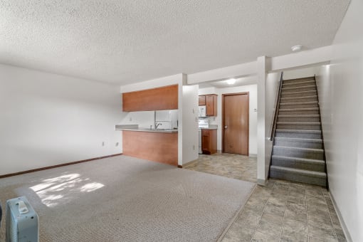 an empty living room with a staircase and a kitchen in the background