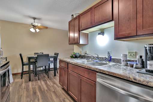 the view of a kitchen and dining room with wood cabinets and a stainless steel sink