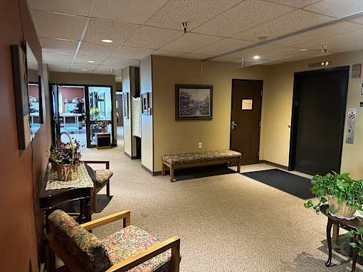 A waiting room with a bench, chairs, and a painting on the wall.