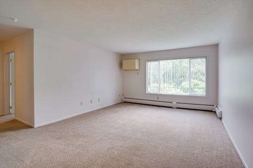 the living room of an apartment with carpet and a large window
