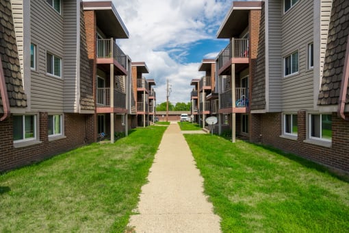 a walkway between two rows of buildings with grass on both sides
