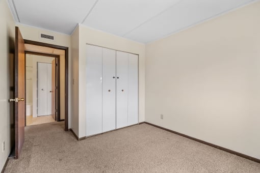 a bedroom with closet doors and carpeting and a door to a closet