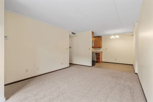 the living room and kitchen of an empty house with white walls and carpet