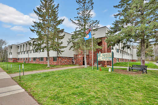 the front of a school building with a green lawn and a bench