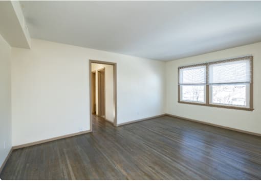 A room with a wooden floor and a window with blinds.