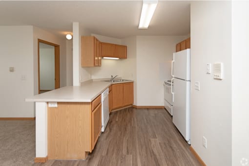 an empty kitchen with white appliances and wood flooring