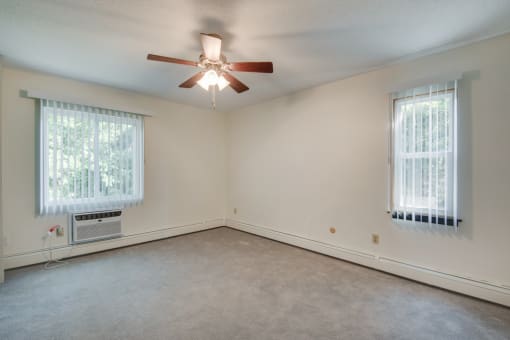 an empty living room with a ceiling fan and two windows