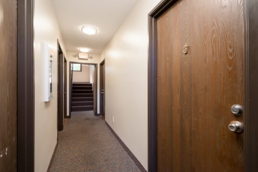 a hallway with wood doors and white walls and a staircase