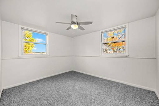 A room with a ceiling fan and two windows.