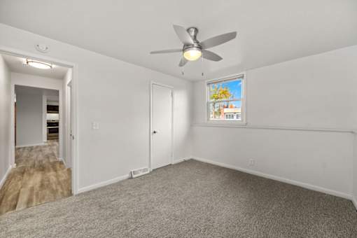A room with a ceiling fan and a window with a view of a garden.