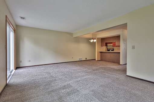 A spacious room with a carpeted floor and a small kitchenette in the corner.