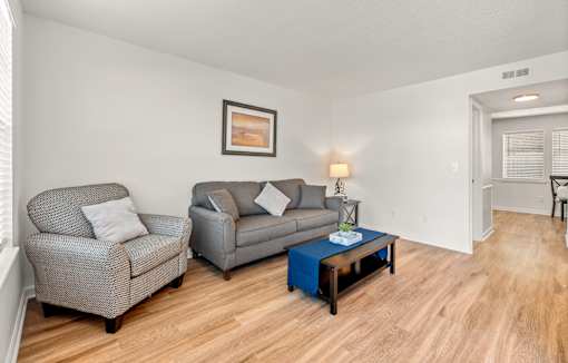 A living room with a grey couch, a grey armchair, a blue coffee table, and a painting on the wall.