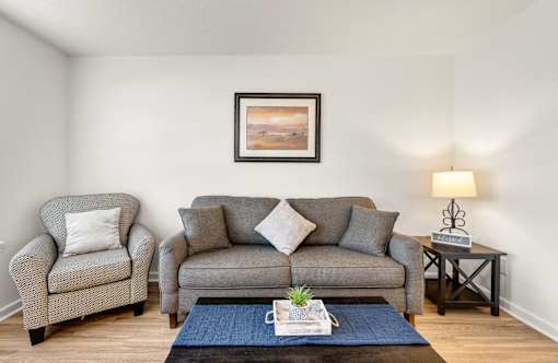 A living room with a grey couch, two armchairs, a coffee table, and a painting on the wall.